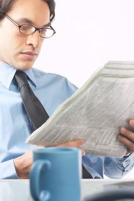 Businessman reading newspaper beside mug of coffee.jpg