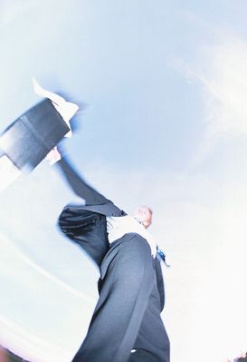View of businessman throwing briefcase against blue sky.jpg