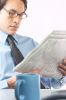 Businessman reading newspaper beside mug of coffee.jpg